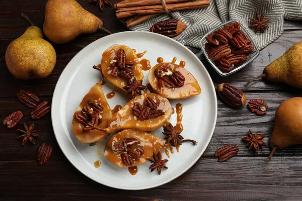 Karamel soslu armutlar, fındıklar ve ahşap masada baharatlar.