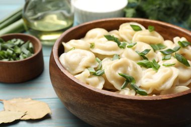 Açık mavi ahşap masada yeşil soğanlı leziz pelmeni, yakın plan.