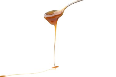 Beyaz arka planda kaşıktan akan lezzetli karamel sosu, yakın plan.