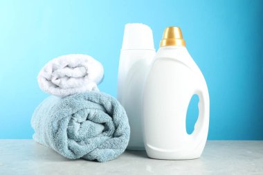 Çamaşır deterjanı şişelerde ve havlularda açık mavi arka planda gri mermer masada.