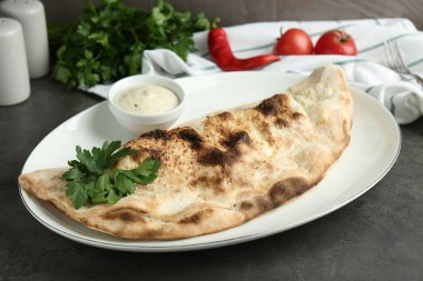 Gri masadaki sosla servis edilen leziz calzone, yakın plan.