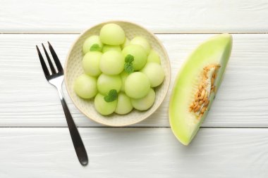 Melon balls in bowl and fresh fruit on wooden table, top view clipart