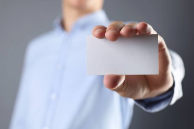 Gri arka planda boş bir kartvizit tutan adam, yakın plan. Tasarım için model