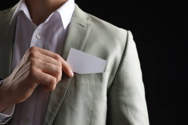 Siyah arka planda ceketinin cebinden boş kartvizit alan adam, yakın plan. Tasarım için model