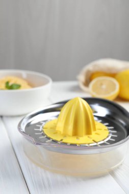 Plastik sıkacağı ve beyaz ahşap masada taze limonlar, yakın plan.