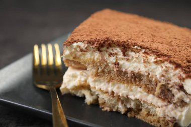 Lezzetli tiramisu ve çatal siyah masada, yakın plan.