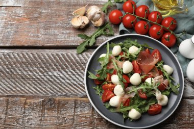 Lezzetli salata roka, mozzarella peyniri, domates ve ahşap masaya konmuş jamon. Metin için boşluk