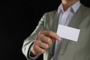 Siyah arka planda boş bir kartvizit tutan adam, yakın plan. Tasarım için model