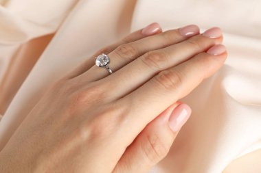 Bej kumaşa karşı değerli taşlı güzel bir yüzük takan kadın, yakın plan.