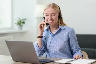 Interpreter in headset working with laptop at table indoors clipart