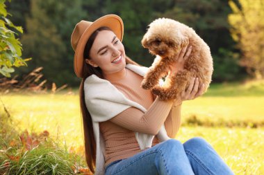 Sonbahar parkında sevimli köpeğiyle gülümseyen kadın.