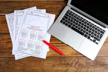 UI tasarımı geliştiriliyor. İnternet sitesi çizimleri, dizüstü bilgisayar ve tahta masa üzerindeki dolma kalem, üst görünüm.