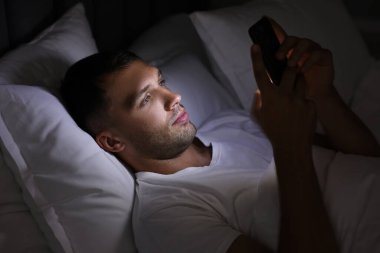 Kötü alışkanlık. Adam gece yatakta akıllı telefon kullanıyor.