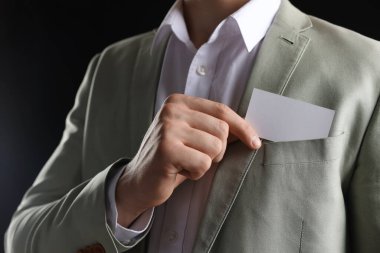 Siyah arka planda ceketinin cebinden boş kartvizit alan adam, yakın plan. Tasarım için model