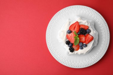 Krem şantili Pavlova keki (kremalı pasta), kırmızı arka planda taze böğürtlen ve nane şekeri, üst manzara. Metin için boşluk