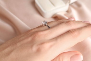 Bej kumaşa karşı değerli taşlı güzel bir yüzük takan kadın, yakın plan.