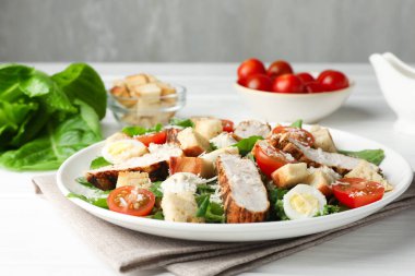 Beyaz ahşap masada tavuklu ve domatesli leziz Sezar salatası.