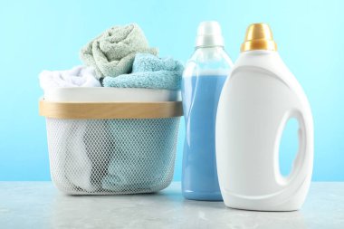 Çamaşır deterjanı şişelerde ve havlularda açık mavi arka planda gri mermer masada.