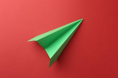 Kırmızı arkaplanda bir el yapımı yeşil kağıt uçak, üst görünüm.
