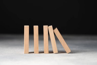 Domino etkisi. Tahta bloklar siyah arkaplana karşı ışık masasına düşüyor, yakın plan