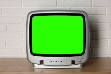 Beyaz tuğla duvarın yanındaki ahşap masada yeşil ekranlı Retro TV seti. Krom anahtar