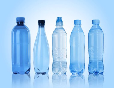 Açık mavi zemin üzerinde su olan farklı plastik şişeler.