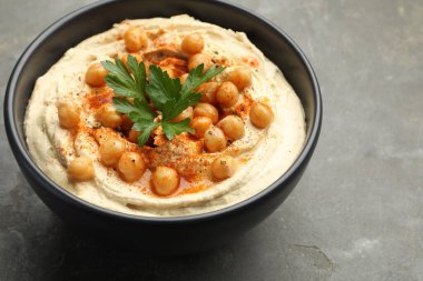 Maydanozlu enfes humus, kırmızı biber ve nohut kasede gri masada, yakın plan.