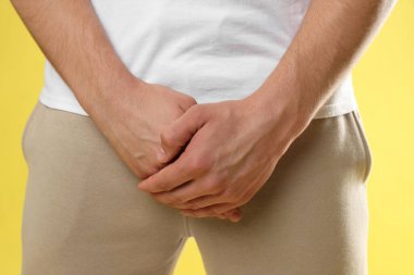 Cinsel yolla bulaşan hastalıklar. Sarı arka planda belirtilerden muzdarip bir adam, yakın plan.