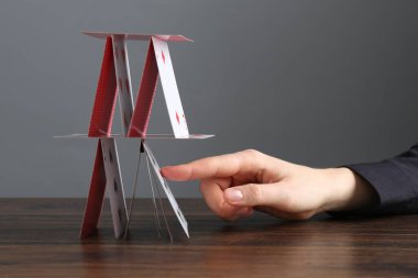 Ahşap masadaki iskambil kağıtlarının olduğu evi yok eden kadın gri arka planda, yakın plan.