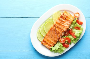 Sebze salatası ve açık mavi ahşap masada limonlu leziz ızgara somon filetosu. Metin için boşluk
