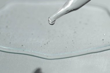 Işık arkaplanındaki pipetten akan kozmetik serumu, yakın plan