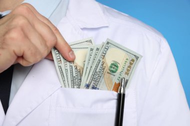 Yozlaşma konsepti. Doktor cebine dolar banknotları koyuyor mavi arka planda, yakın plan