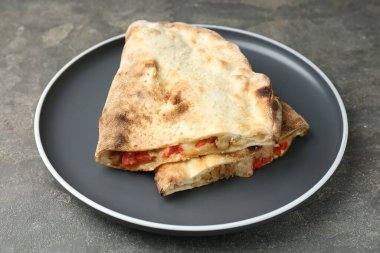 Gri desenli masada etli, peynirli ve domatesli yarım porsiyon leziz calzone.