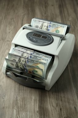 Tahta masanın üzerinde dolar banknotları olan para sayma makinesi.