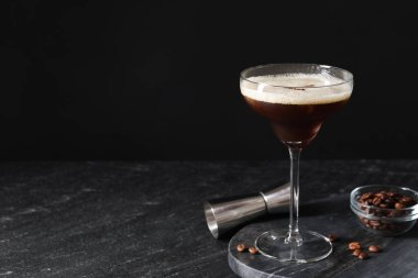 Bir bardak nefis espresso martini, jigger ve kahve çekirdekleri koyu dokulu masada, yakın plan. Metin için boşluk