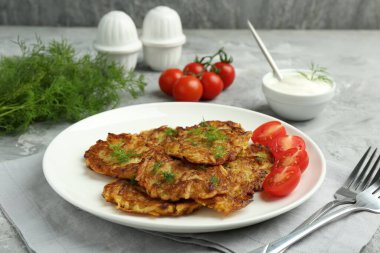 Gri masada servis edilen taze domatesli leziz patates krepleri.