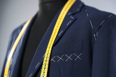 Semi-ready jacket and measuring tape on mannequin against gray background, closeup clipart