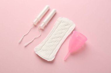 Açık pembe arka planda adet pedi, fincan ve tamponlar.