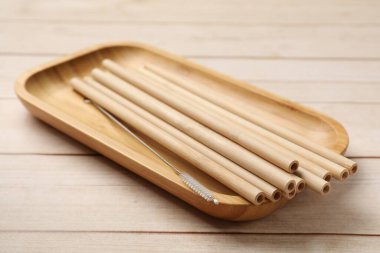 Bamboo drinking straws and cleaning brush in tray on wooden table, closeup