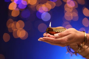 Diwali kutlaması. Mavili arka planda yanan diya lambası tutan kadın, yakın plan.