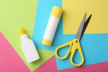 Glue, colorful paper and scissors on pink background, flat lay