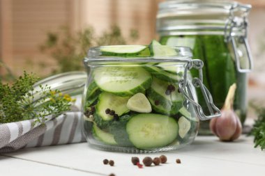 Ev yapımı turşu. Kavanozda taze salatalıklar, biberler ve beyaz ahşap masada dereotlar, yakın plan.