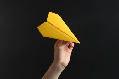 Siyah arka planda sarı kağıt uçaklı kadın, yakın plan.