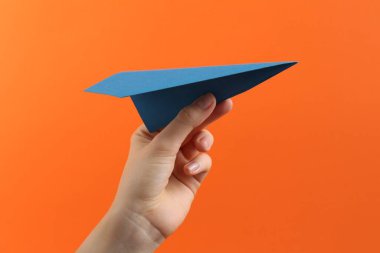 Turuncu arka planda mavi kağıttan uçağı olan kadın, yakın plan.