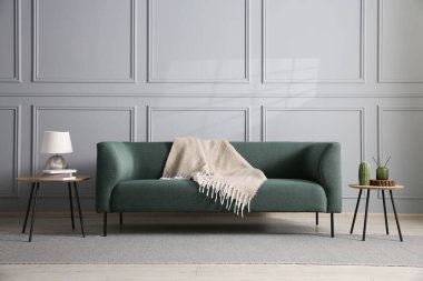 Rahat bir kanepe ve gri duvarın yanındaki yan masalar.