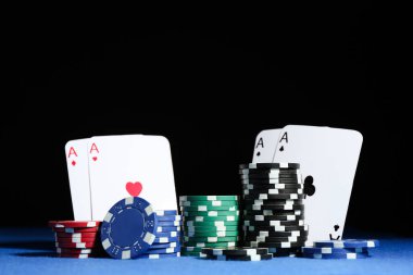 Koyu arkaplana karşı mavi masada kart ve poker çipleri oynamak