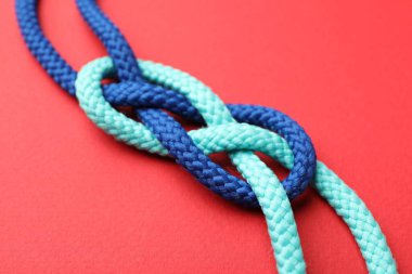 Kırmızı arka planda düğümlenmiş renkli ipler, yakın plan. Birlik kavramı