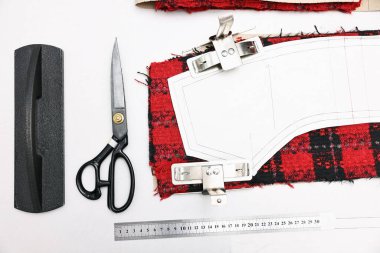 Beyaz masadaki kumaş parçaları, ölçümler, makas ve diğer aletler
