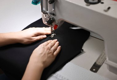 Profesyonel atölyede dikiş makinesiyle çalışan kadın, yakın plan.