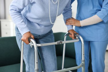 Hemşire üst düzey bir kadına içeride yürüme iskeletinde yardım ediyor, yakın plan.